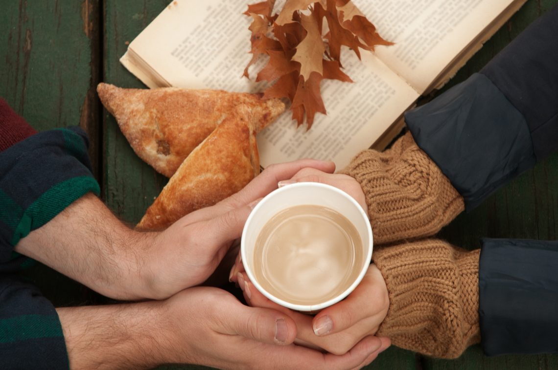 Loving couple holding hot coffee in hands on autumn background