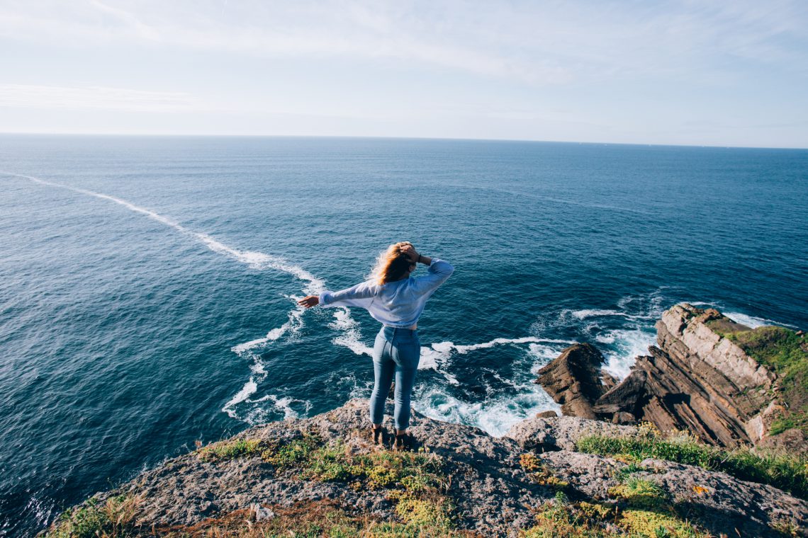 Female traveller overlooks ocean cliffs