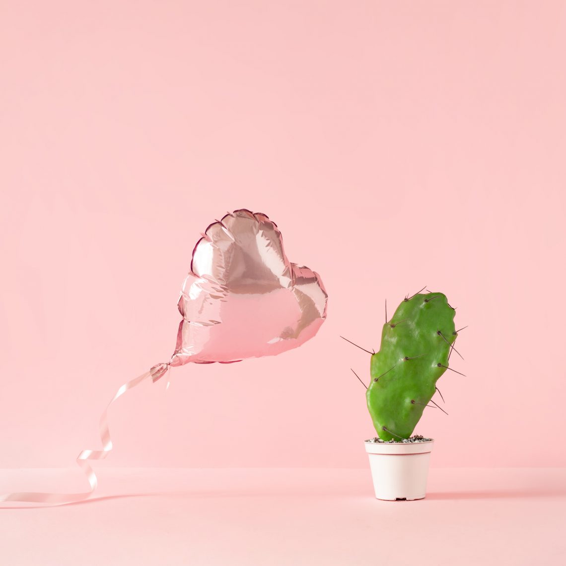 Heart shaped foil balloon with cactus plant and pink background.