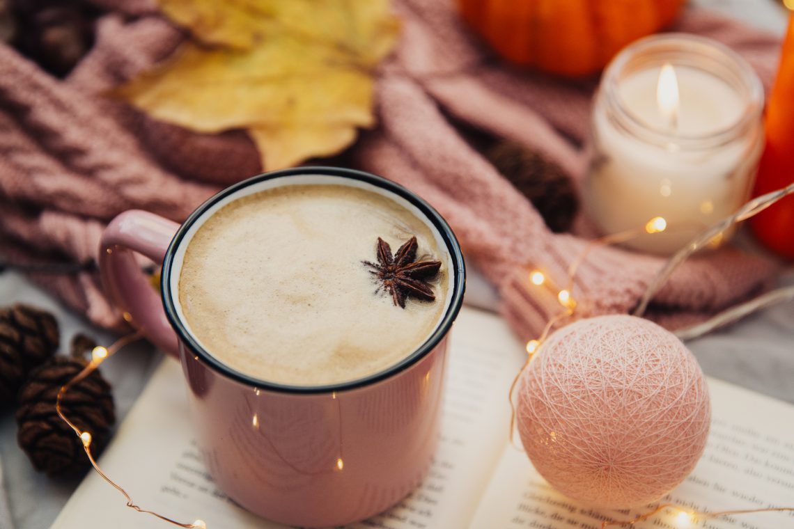 Cup of coffee, leaves, book and candles. Spending autumn weekend in the cozy bed.