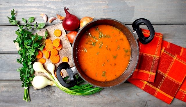 Top view on pot of tomato soup and fresh vegetables on old wooden table