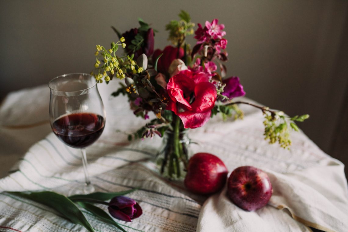 Бокал с вином, цветы и яблоки на скатерти фото