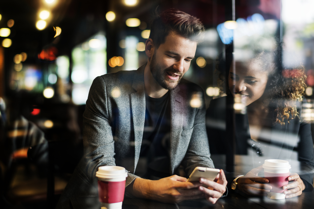 Фото мужчина и женщина сидят в кофейне и смотрят на экран смартфона