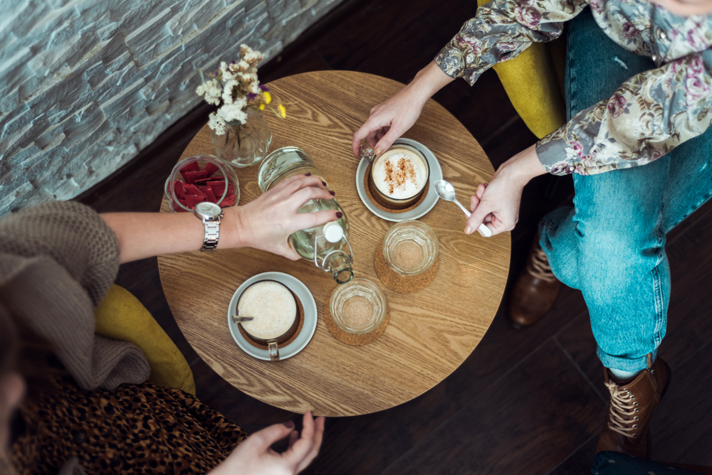 Фото сверху стол в кафе с кофе и цветами руки посетителей