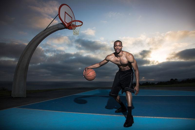 Young man playing basketball in a park with dramatic sky on background 