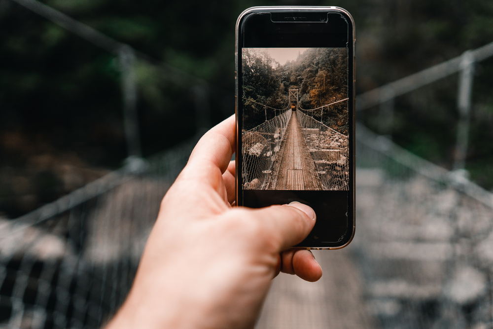 Фотографія чоловік знімає на смартфон підвісний міст