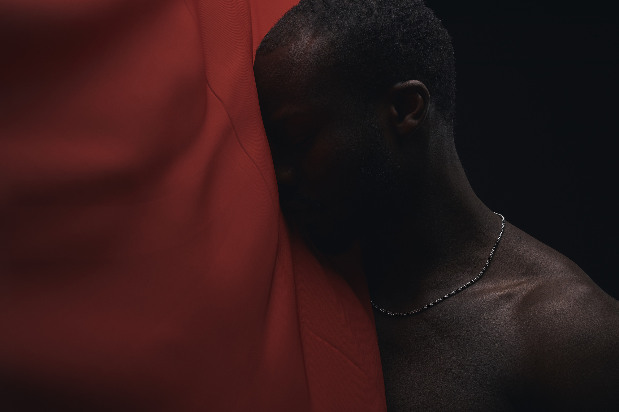 Art portrait of afro man. Man's head behind red fabric, black background. Dark key. Sensual