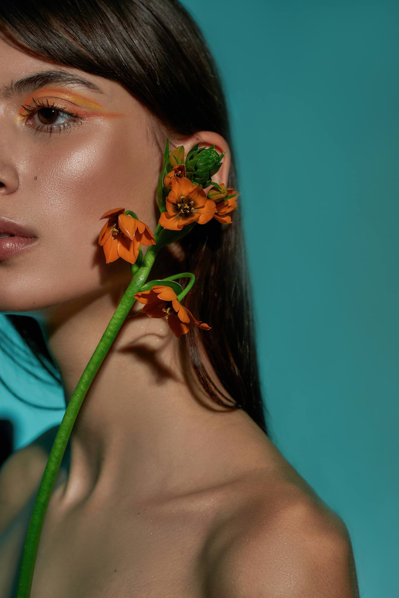 Cropped photo of a woman model reaching to her ear with a flower bud
