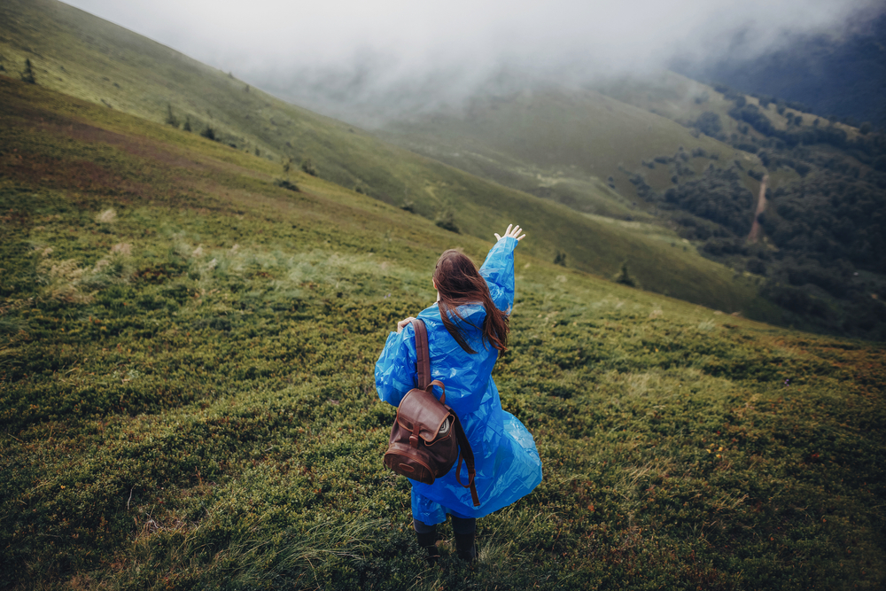 Фотографія дівчини з рюкзаком у дощовику в горах