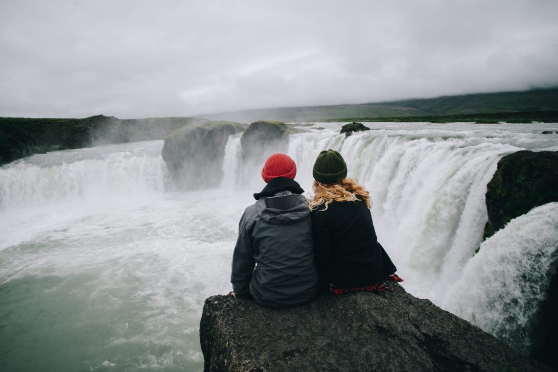 Фотографія пара сидить на скелі перед водоспадом