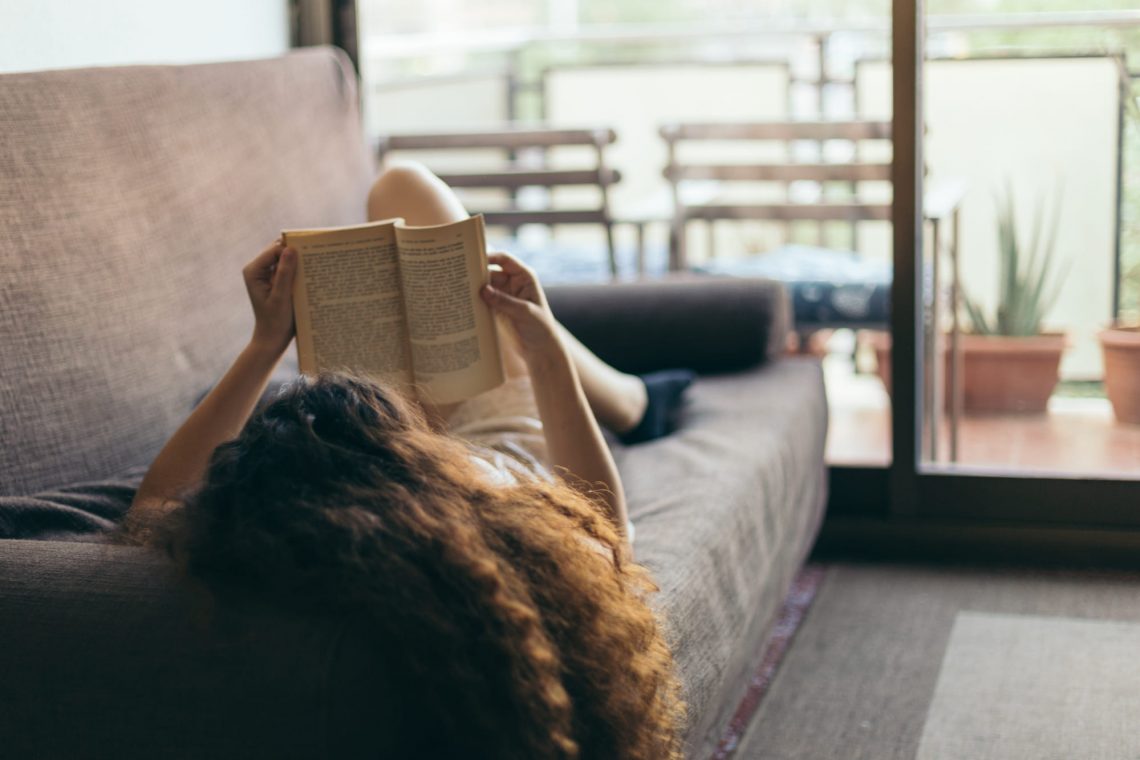 Фотографія жінки, яка читає книгу на дивані