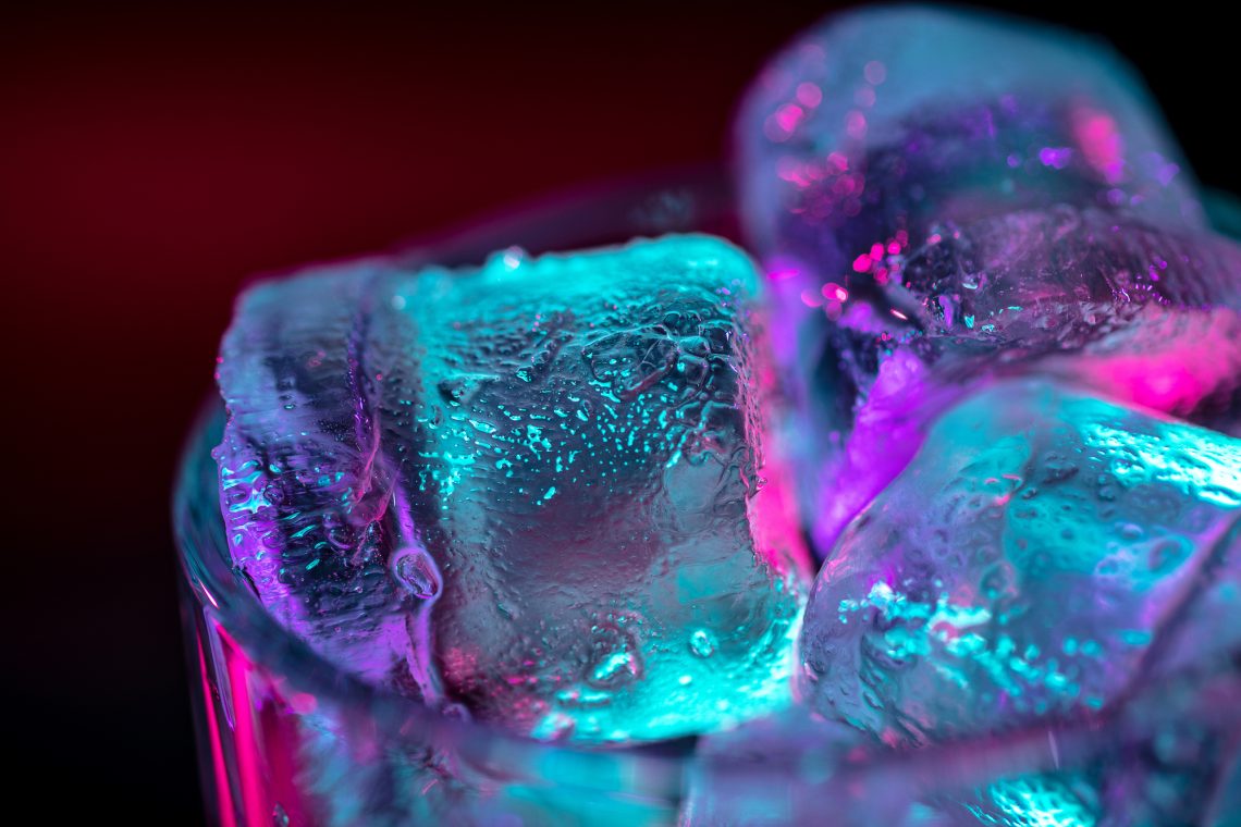 Close up of ice cubes in glass of alcoholic cocktail, beverage, drink in multicolored neon light