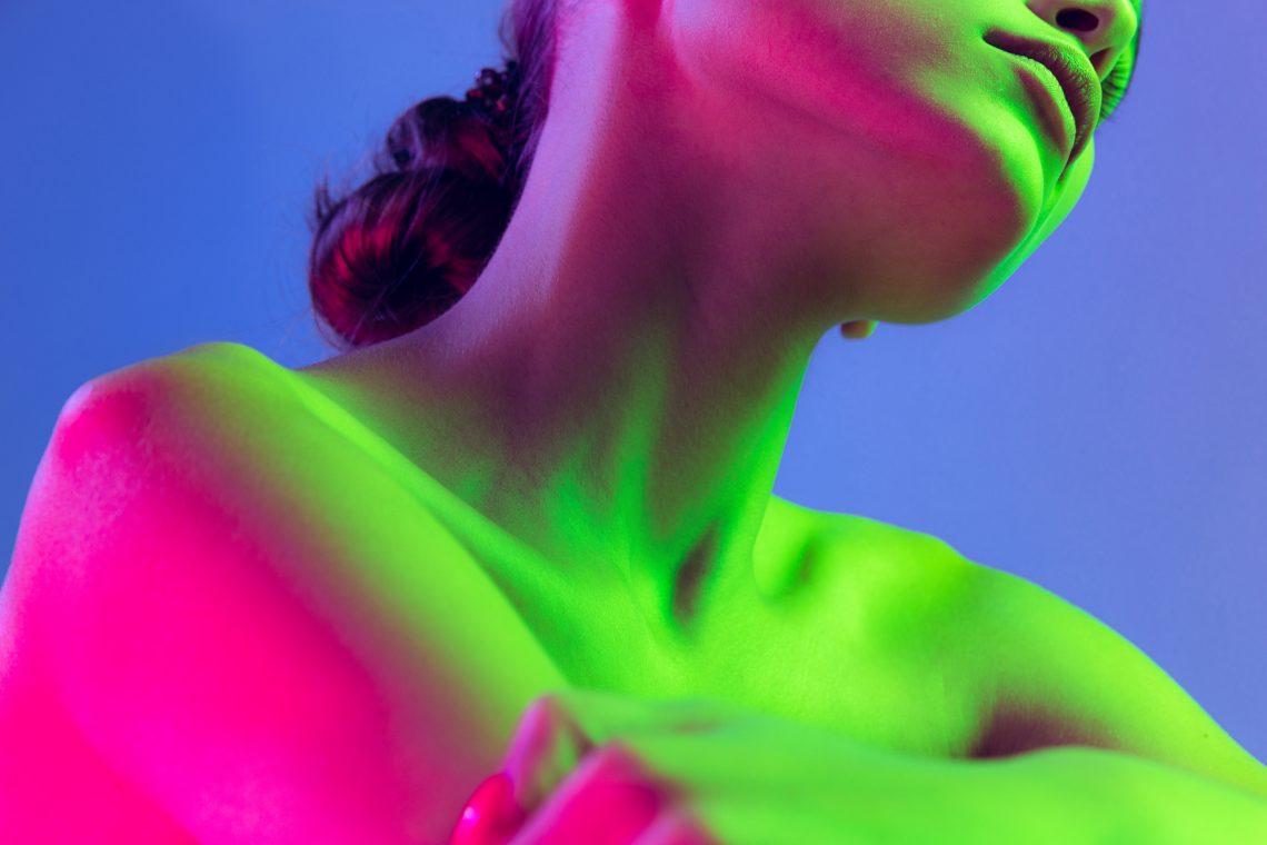 Close up female neck, collarbones and shoulders in pink neon light over dark background. Natural beauty, fitness, diet, spa, aesthetic cosmetology