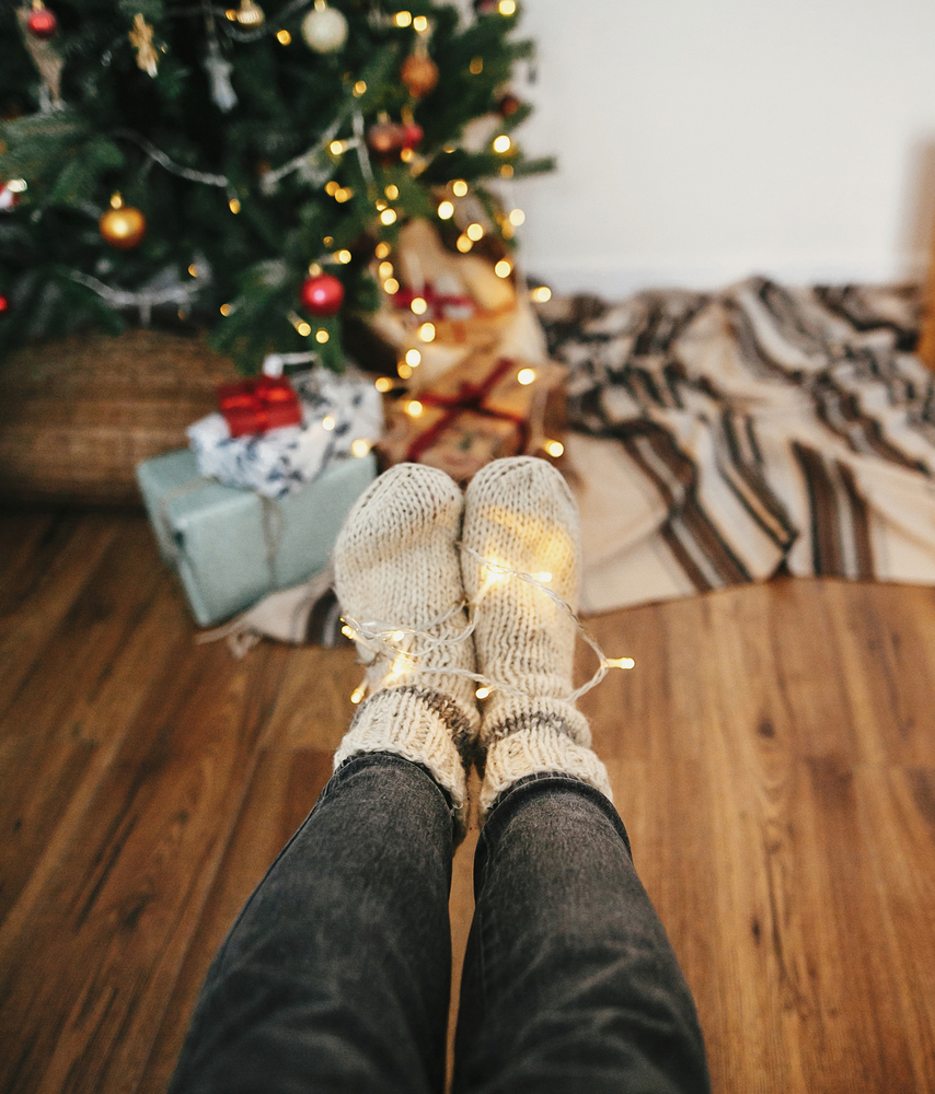 Фотографія ноги у вовняних шкарпетках на фоні новорічної ялинки