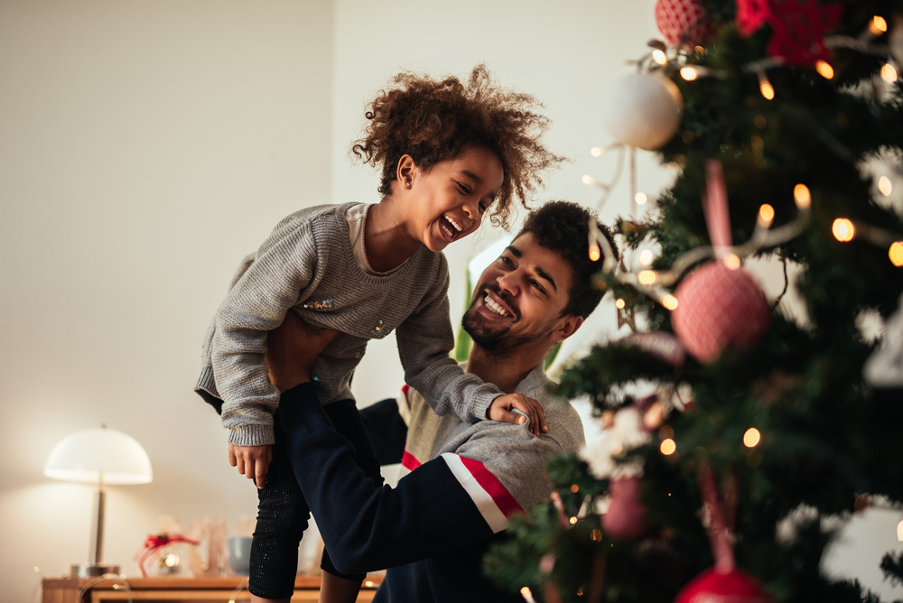 Фотографія темношкірий чоловік з донькою біля новорічної ялинки