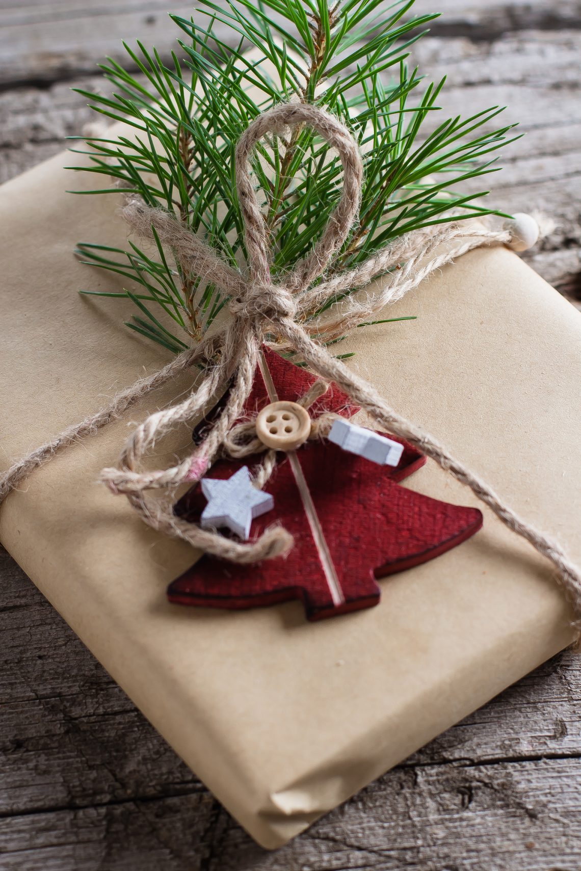 Holiday christmas gift box. Christmas present with fir branch and red wooden tree toy decoration on wooden table background.