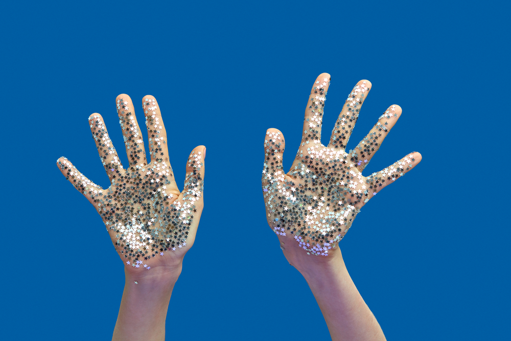 Woman's hands with bright silver glitter stars on a blue