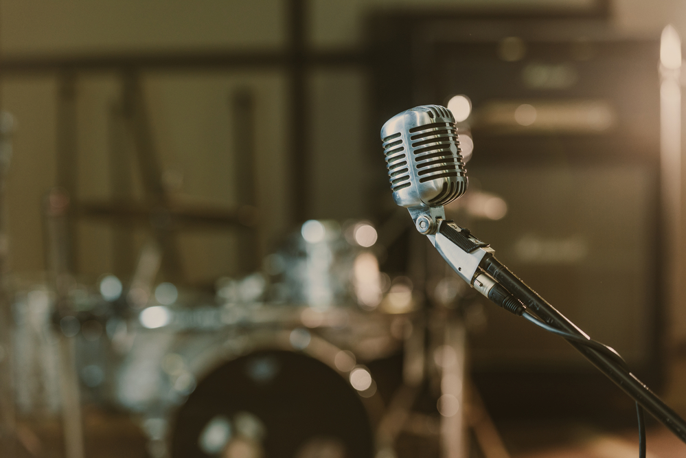 Close-up shot of vintage microphone on stand against blurred drum set