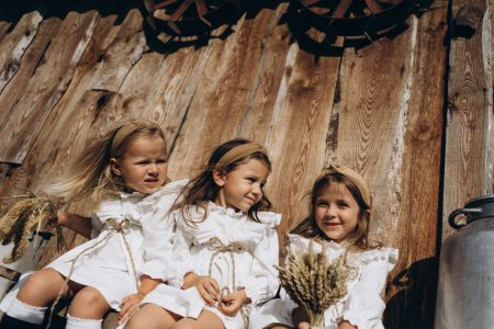 Фото маленькі дівчата, одягнені в старовинні сукні, сидять біля дерев'яного паркану