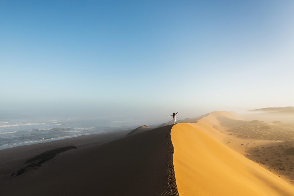 Woman walking on top of huge sand dune in Morocco Sahara desert.