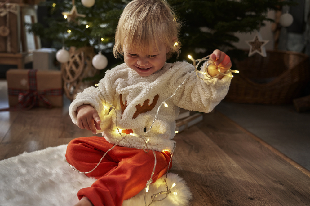 Toddler sitting on floor and playing with Christmas lights