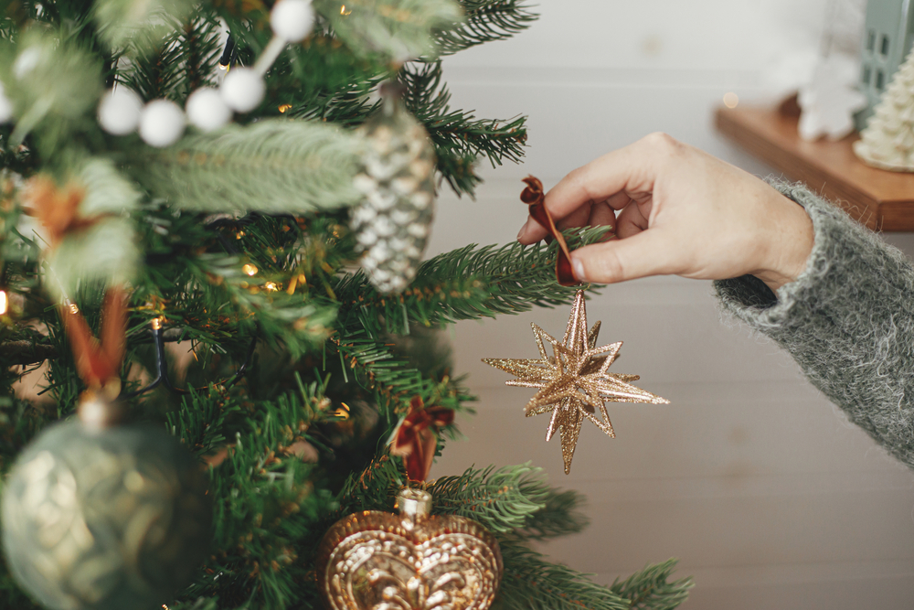 Hands decorating christmas tree with stylish bauble in atmospher
