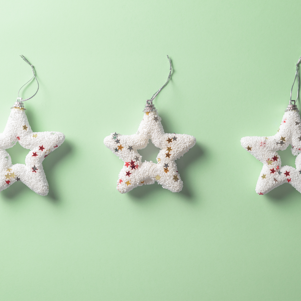 Фото три білі ялинкові іграшки у формі різдвяних зірок на пастельно-зеленому фоні