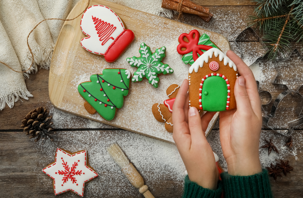 Woman holding delicious homemade Christmas cookie at wooden table, top view