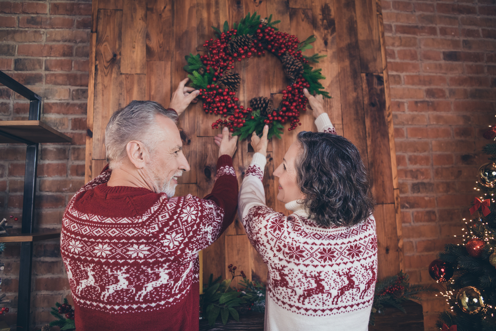 Photo of bonding couple hang mistletoe wreath together wear deer print pullover in decorated home indoors