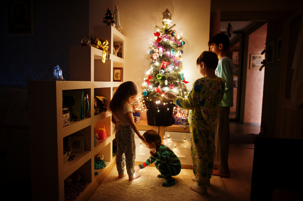 Kids looking on Christmas tree with shining garlands on evening
