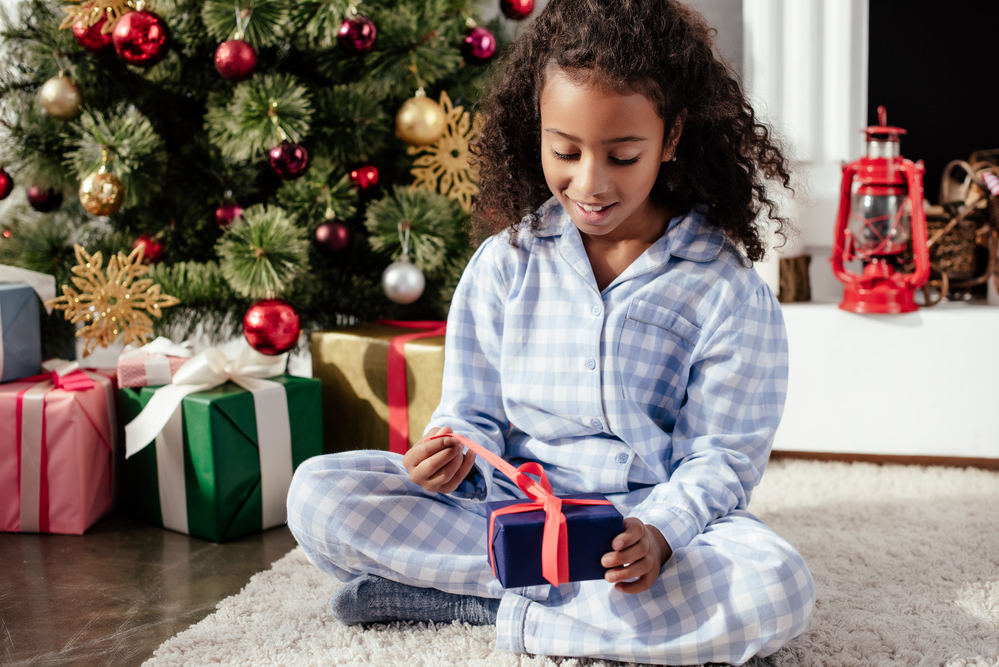 Фото темношкіра дівчинка у піжамі відкриває різдвяний подарунок