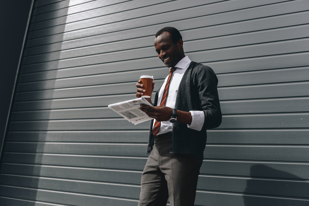 Photo stylish african american businessman reading newspaper and holding coffee to go outdoors