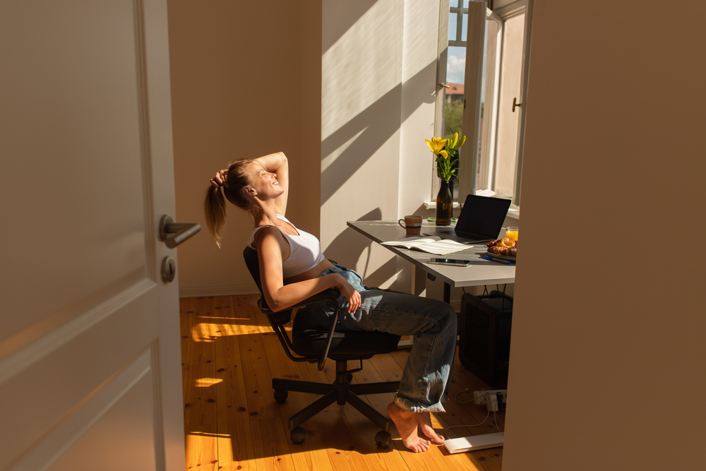 Фото молода жінка посміхається, сидячи за робочим столом у променях сонця