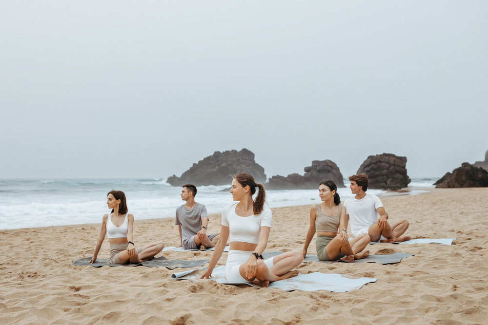 Summer yoga training. Group of men and women practicing yoga at the beach on ocean shore, sitting on fitness mats