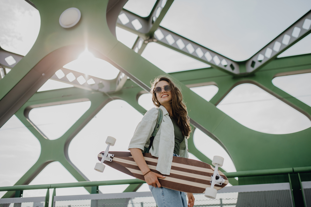 Young woman walking on city bridge with skateboard. Youth culture and commuting concept.