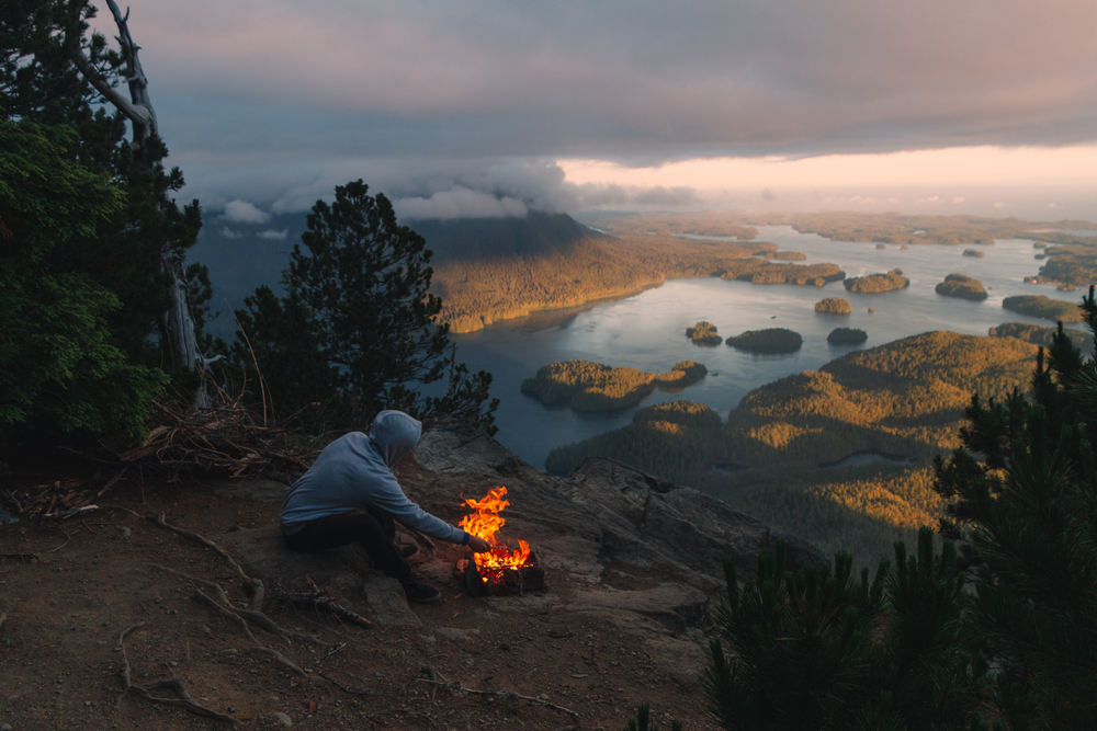 Man sitting on the rim with campfire above coastal view with isl
