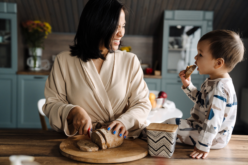 Photo happy mother making fun with her son while cutting bread at home